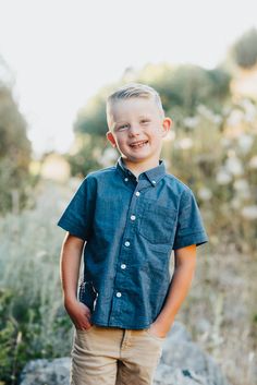 a young boy is standing in front of some rocks and grass smiling at the camera