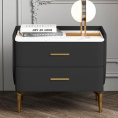 a nightstand with a lamp and books on it next to a gray wall in a living room