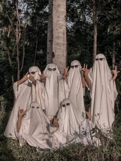 five people in white cloths standing next to a tree with their hands raised up