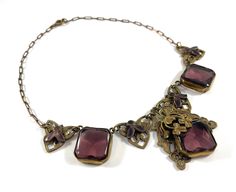 Vintage Necklace Czech Amethyst Rare Collectible This exquisite antique necklace is very unique with wonderful details and a spectacular Czech design made of brass filigree with Large Amethyst Purple glass stones and purple enamel. The three large Amethyst glass stones are square and faceted in the back but smooth in the front to show off the sparkle and the stunning color. Each stone is set into an open back bezel setting with fine sawtooth edging. the center stone is adorned with layers of brass filigree that frame and decorate the top of the stone with brass floral and three leaf clover shapes. The two stones on the sides alternate with triangular brass filigree links that have a lovely open work design accented by purple enameled leaves. The brass chain is a paper clip style and closes Three Leaf Clover, Ring Shapes, Antique Necklace, Vintage Purse, Large Ring, Amethyst Purple, Wedding Jewellery Necklace, Purple Glass, Heart Locket