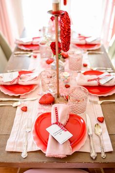 the table is set for valentine's day with pink and red plates, silverware, and napkins