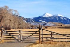 a wooden gate in the middle of a grassy field with mountains in the back ground