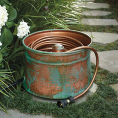 an old rusty bucket with water coming out of it sitting on the ground next to some white flowers