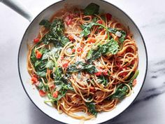 a pan filled with pasta and spinach on top of a marble countertop next to a spoon