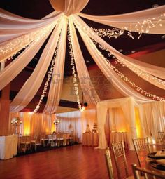 the inside of a banquet hall decorated with white drapes and lights