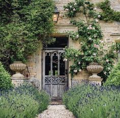 the entrance to an old stone house surrounded by flowers and greenery