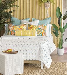 a bed with lots of pillows on top of it next to a potted plant