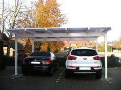 two cars are parked under an awning in the driveway, one is white and the other is black