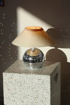 a lamp sitting on top of a block of cement next to a mirror ball shade