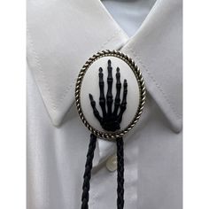 Add a touch of Western charm to your outfit with this unique bolo tie from FANCY FOX BOUTIQUE. The tie features a striking skeleton skull hand design, crafted from RESIN CAMEO, set against a black leather background. The metal components of the tie are silver in color, and the metal purity is unknown. This handmade piece is perfect for a variety of occasions including weddings, parties, and graduations. It also makes a great gift for Father's Day, Christmas, or birthdays. The tie has a Southwest Goth Bolo Tie, Elegant Concho Bolo Tie, Elegant Adjustable Halloween Jewelry, Gothic Wedding Party, Black Leather Background, Pins Hat, Leather Background, Black Suit Wedding, Skeleton Skull