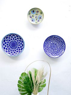 three bowls with designs on them sitting next to a potted plant