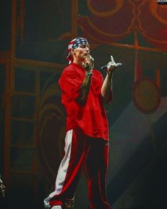 a man standing on top of a stage holding a microphone in his right hand and wearing a bandana