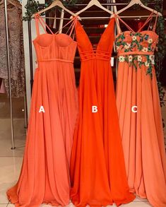 three bridesmaids in orange dresses hanging on racks