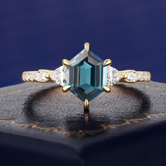 an emerald and diamond ring sits on top of a black leather book in front of a blue background