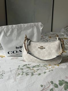 a white coach purse sitting on top of a bed