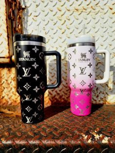 two travel mugs sitting next to each other on top of a table in front of a wall