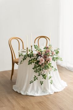 two chairs and a table with flowers on it, in front of a white wall