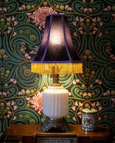 a lamp sitting on top of a wooden table next to a wallpapered wall