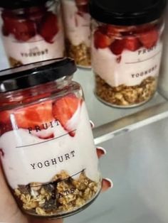 a person holding a jar filled with yogurt and strawberries in front of other jars