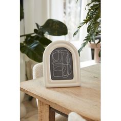 a white clock sitting on top of a wooden table next to a potted plant