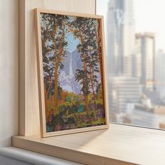 a painting on a window sill in front of a cityscape with skyscrapers