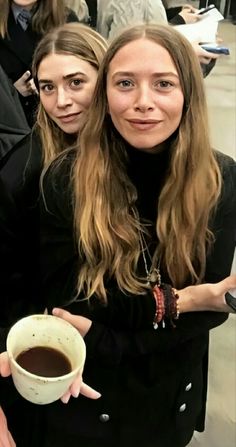 two women are posing for the camera while holding a cup of coffee in their hands