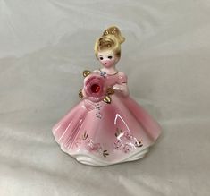 a pink glass figurine with a blonde haired girl in a dress holding a flower