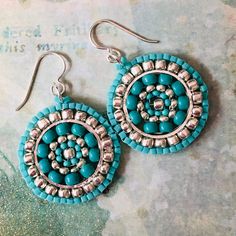 a pair of earrings with turquoise beads and silver accents on top of a piece of paper