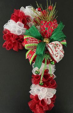 a red and white christmas wreath with bells on it's side, hanging from a black wall