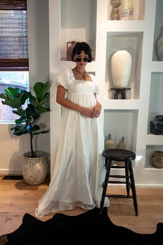 a woman in a white dress standing next to a plant