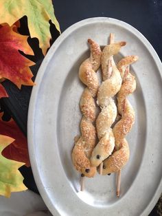 several skewered food items on a white plate with autumn leaves in the background