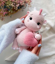 a hand holding a small pink crocheted cat with big ears and tail, in front of flowers