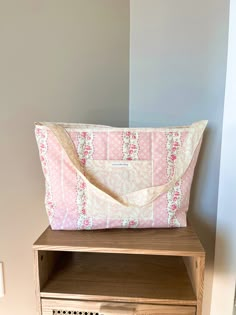 a pink and white purse sitting on top of a wooden table next to a drawer