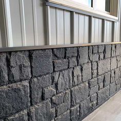 a wall made out of black rocks next to a building with a window on the side