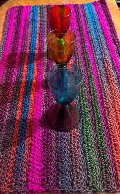 three glasses are sitting on top of a placemat that is knitted with multicolored yarn