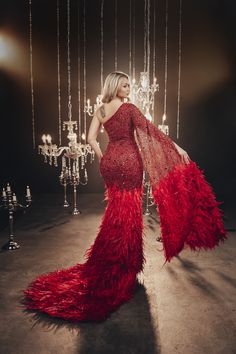 a woman in a red dress with feathers on the floor and chandelier behind her