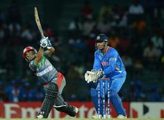 a cricket player hitting the ball with his bat while another man watches from behind him