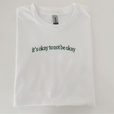 It’s Okay To Not Be Okay White Embroidered Relaxed Fit T-shirt, White T-shirt With Embroidered Logo For Spring, White Embroidered T-shirt With Relaxed Fit, White Casual T-shirt With Embroidered Text, Casual White T-shirt With Embroidered Text, Trendy White Embroidered T-shirt, White Embroidered Text T-shirt For Spring, White Everyday Top With Embroidered Text, White Tops With Embroidered Text For Everyday