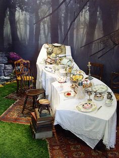 a table set up with tea cups and saucers on it in front of a forest mural