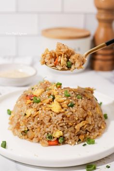 a white plate topped with fried rice and veggies next to a wooden spoon