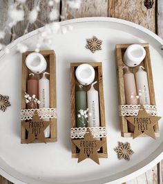 three candles in wooden boxes with tags on them sitting on a white tray next to snowflakes