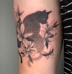 a black cat sitting on top of a flowery branch with leaves and flowers around it