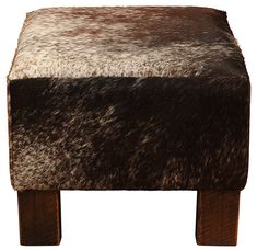 a brown and white cowhide footstool sitting on top of a wooden table