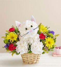 a basket filled with white and yellow flowers next to a pink cat figurine