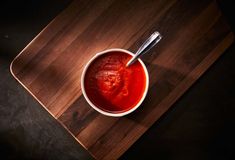 a bowl filled with sauce on top of a wooden cutting board next to a spoon