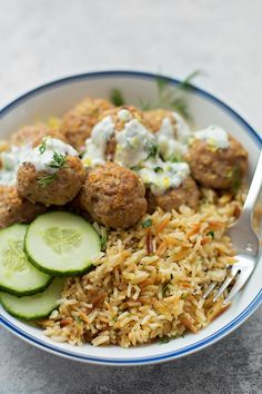 a bowl filled with rice, cucumber and meatballs next to a fork