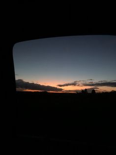 the sun is setting over an open field with trees in the distance as seen through a car window