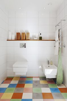 a white bathroom with multicolored tiles on the floor and shelves above the toilet