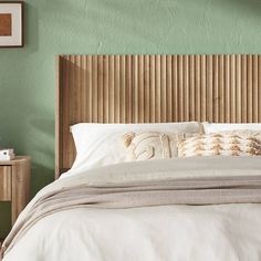 a bed with white linens and pillows in a green walled room, next to a wooden headboard