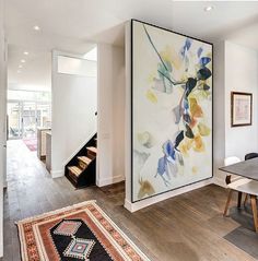 a large painting hanging on the wall next to a dining room table with chairs and rug